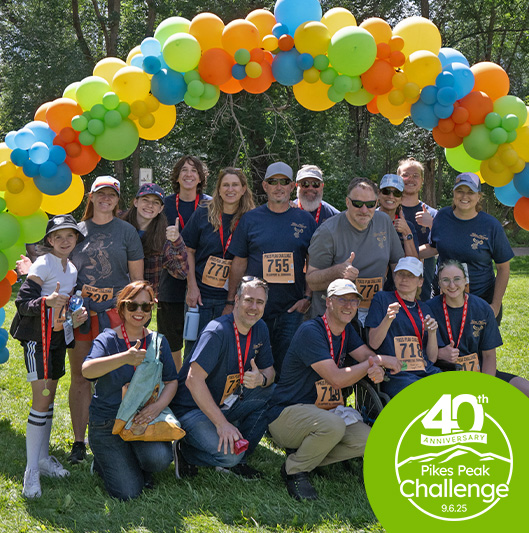 Large group of people under balloon arch at the Manitou Walk, with a 40th Anniversary logo for Pikes Peak Challenge in the bottom corner.
