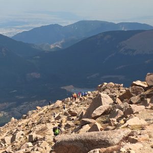 Summit of Pikes Peak with hikers coming up the trail and mountains in the distance.